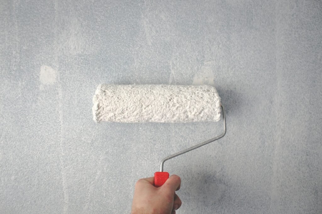 pexels-photo-1669754-1669754 A person's hand using a paint roller to apply white paint on a wall.